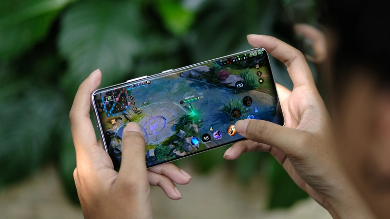 Game thủ trẻ cầm smartphone chơi Liên Quân Mobile với nụ cười chiến thắng.